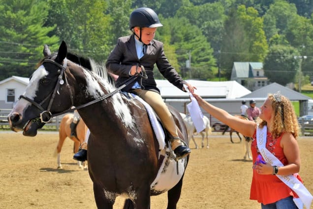 Child on horseback receiving award from woman.